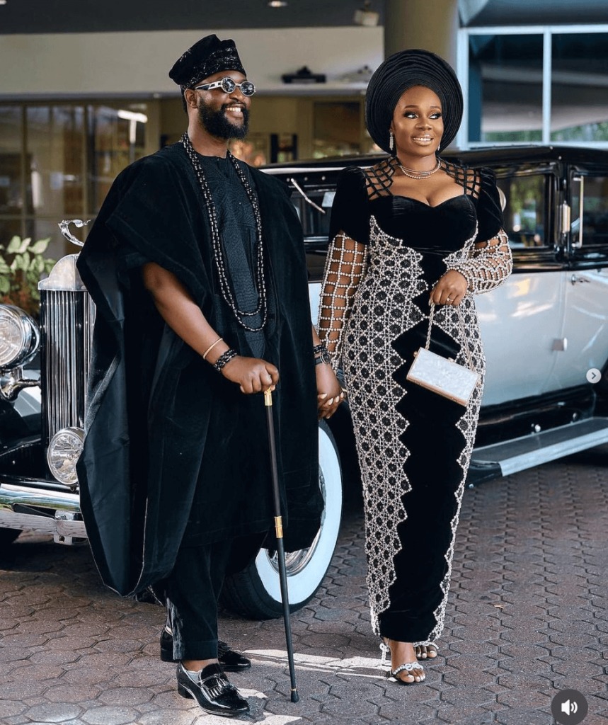 In the tapestry of love and tradition, this couple's wedding attire stood as a vivid expression of their journey. The groom, resplendent in a beautifully tailored black Yoruba Agbada, exuded charisma and grace. Paired with polished black shoes and African beads, he radiated an air of regality that was nothing short of captivating. The bride, equally enchanting, donned an exquisite African attire in the harmonious colors of black and silver. Her dress shimmered with elegance, a reflection of her radiant smile. The ensemble was completed with a black gele that framed her face like a crown and silver shoes that mirrored the twinkle in her eyes. Together, their attire was more than just clothing; it was a statement, a celebration, and a symbol of their love. Their wedding day, a regal affair, was a testament to the beauty of tradition and the richness of their shared journey.